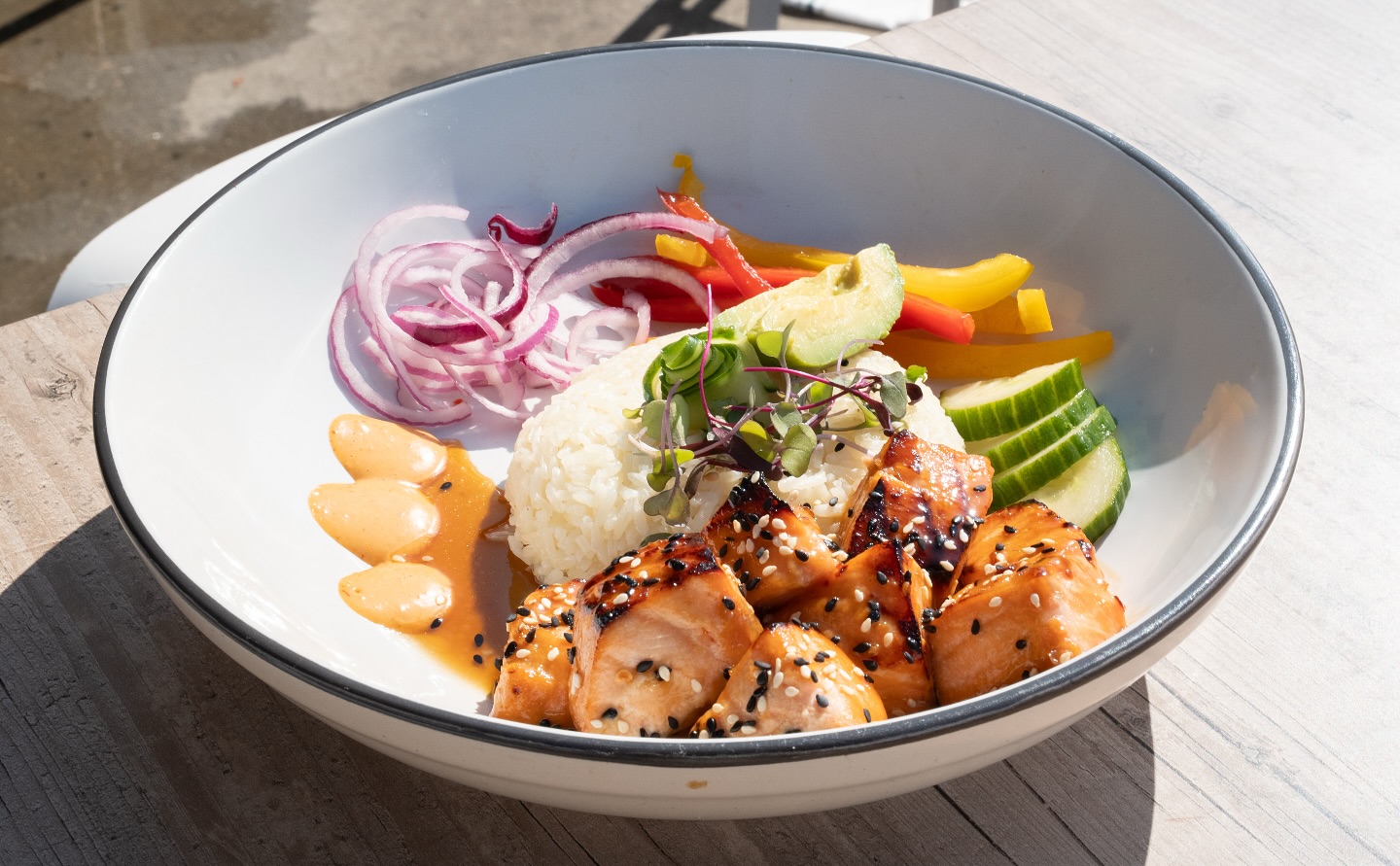 a white bowl with black trim containing a dish with rice, vegetables, and meat