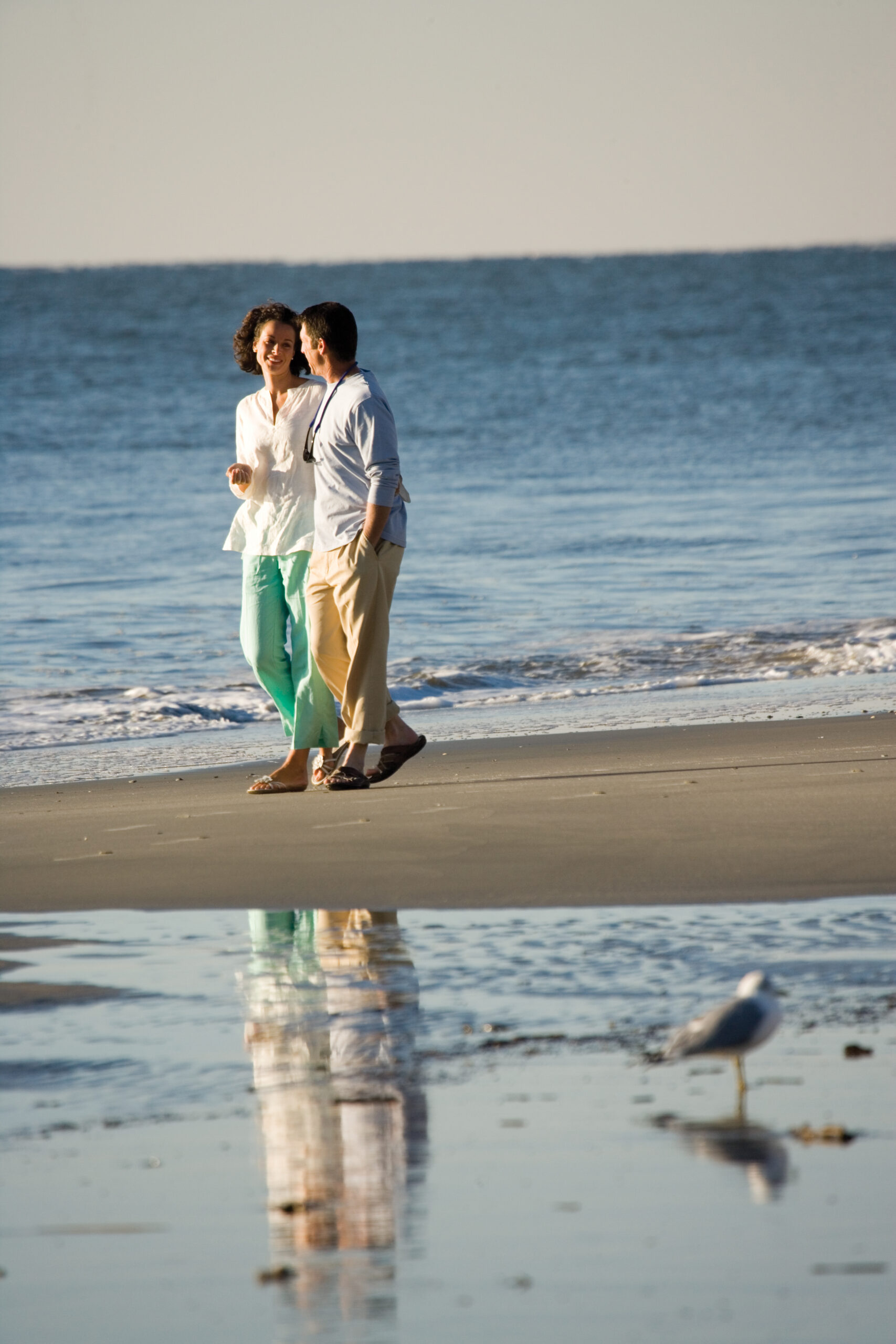 A couple holding hands and walking together on a sandy beach next to the ocean