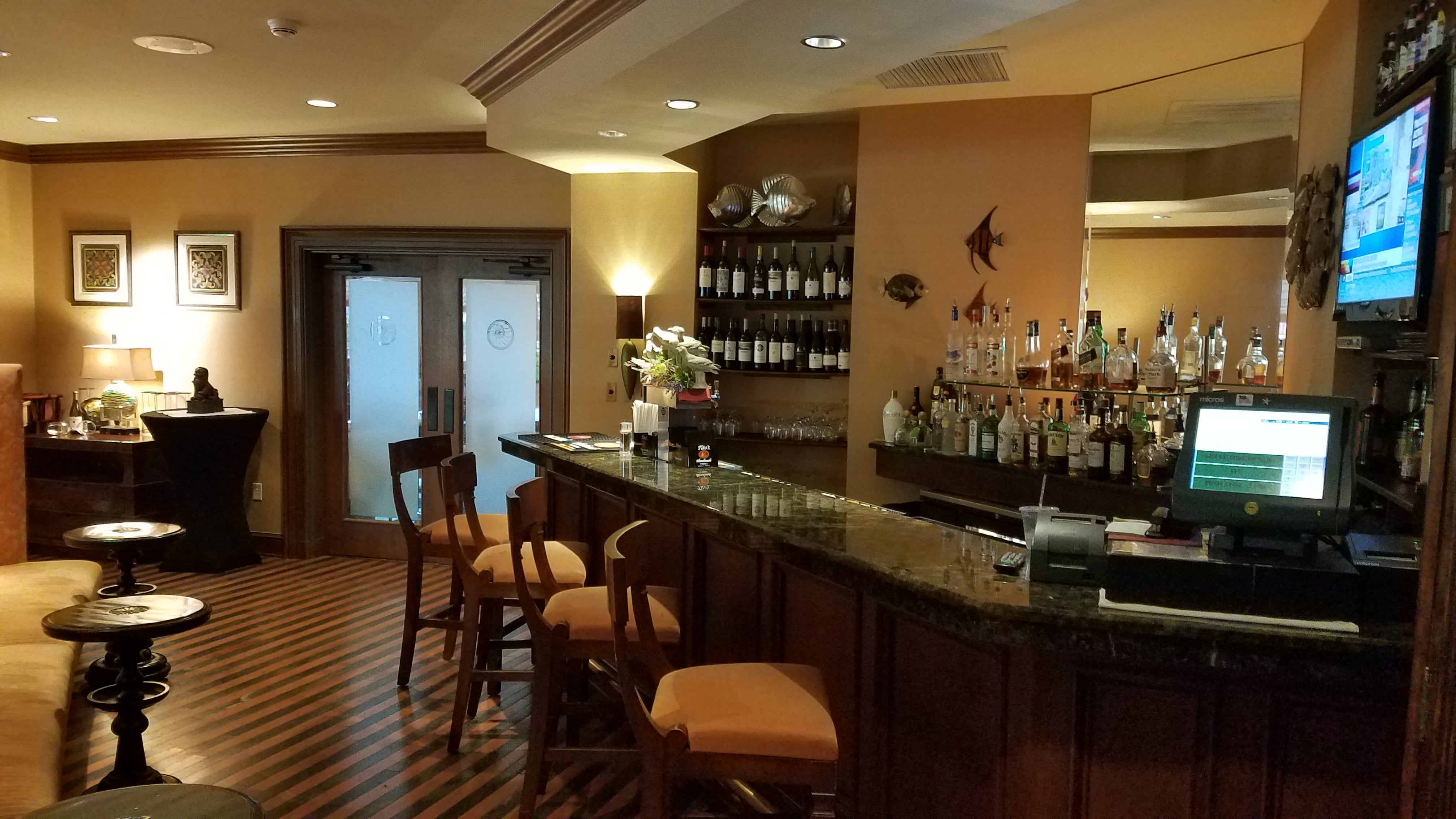A dimly lit bar with a granite countertop, several stools, and a large selection of liquor and bottles on shelves.