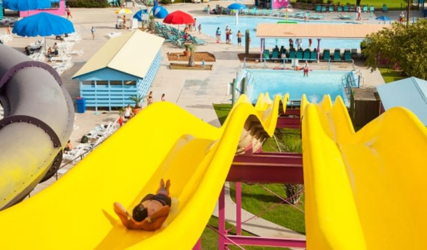 The tourists enjoy sliding on water slides with a large swimming pool and people enjoying a sunny day.