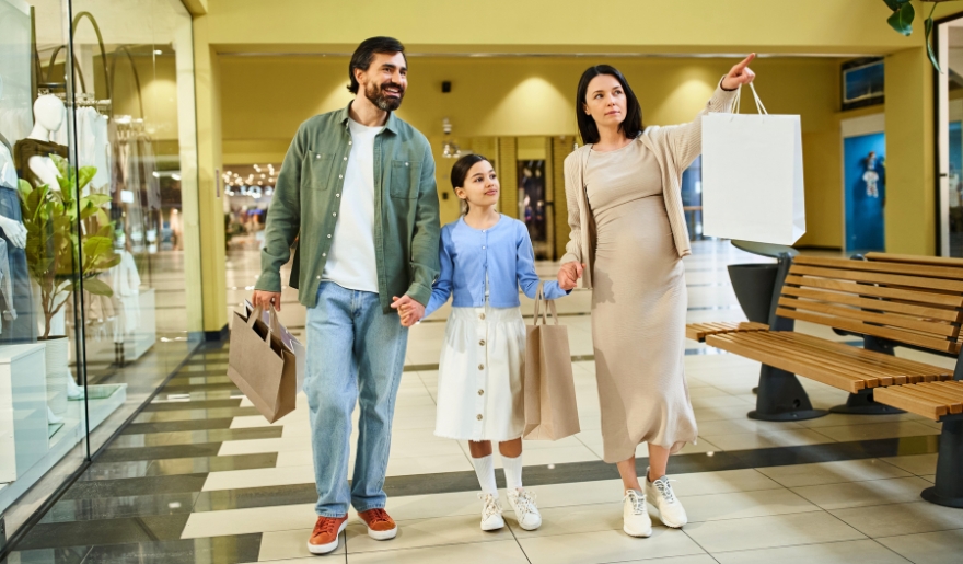 A family strolls through a mall, carrying shopping bags, enjoying a day out at Barefoot Landing in Myrtle Beach.