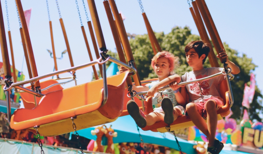 Two children joyfully swinging at a carnival, surrounded by colorful attractions at Myrtle Beach for kids.