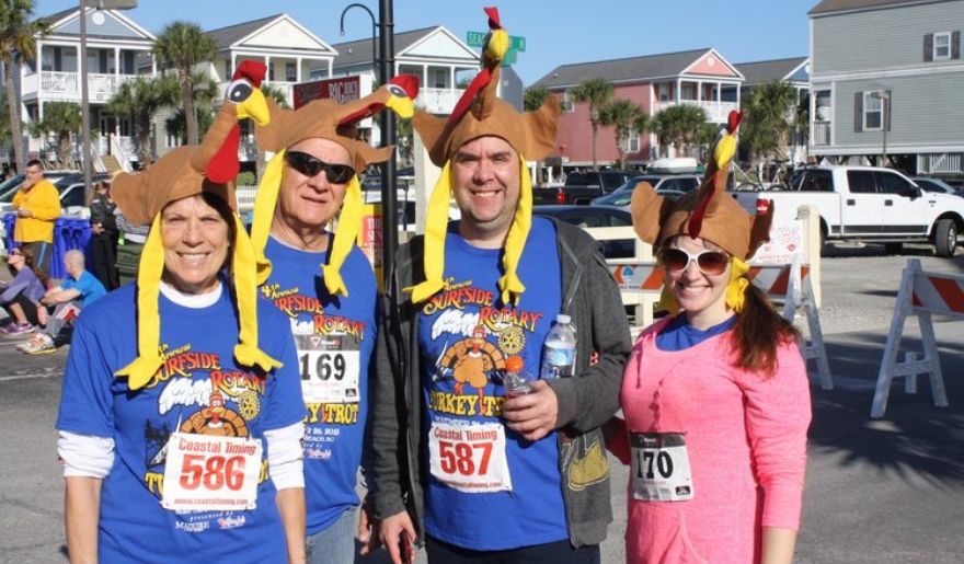 Four friends sporting fun turkey hats, celebrating the Turkey Trot race in Myrtle Beach with smiles and excitement.