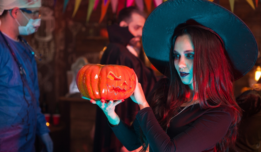 A woman dressed as a witch stands with a pumpkin, enjoying Halloween festivities in Myrtle Beach during October.