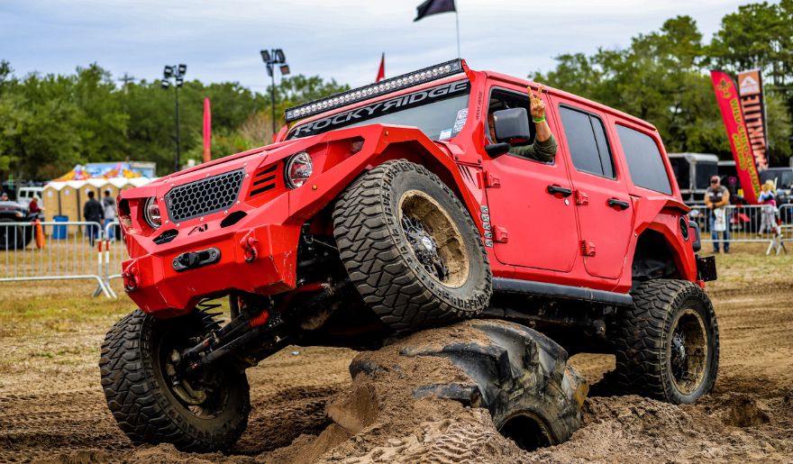 A red jeep navigates through muddy terrain at Myrtle Beach during the month of October, showcasing adventurous driving.