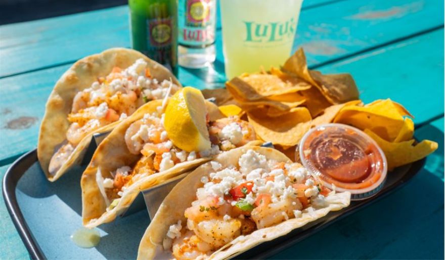 Three tacos on a blue plate accompanied by chips and a drink, showcasing a delightful dining experience in Myrtle Beach.