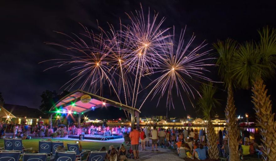 Colorful fireworks illuminate the night sky above the water, enhancing the festive atmosphere of Myrtle Beach's Christmas lights.