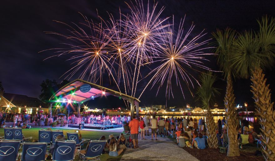 Colorful fireworks illuminate the night sky, with people enjoying the view from Barefoot Landing.