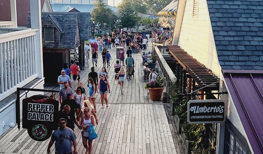 A bustling crowd strolls along the boardwalk at Barefoot Landing, showcasing the vibrant shopping scene of Myrtle Beach.