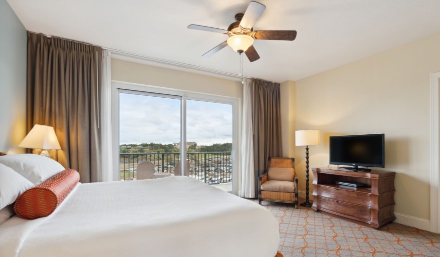 A cozy hotel room featuring a bed, television, and a balcony overlooking the scenic views of Myrtle Beach, perfect for unwind after Myrtle Beach Shopping.