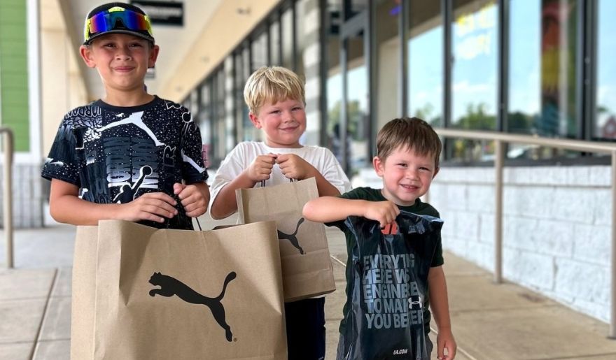 At Tanger Outlet Myrtle Beach, three boys show off their Puma shoe bags, highlighting a fun and rewarding Myrtle Beach shopping experience.