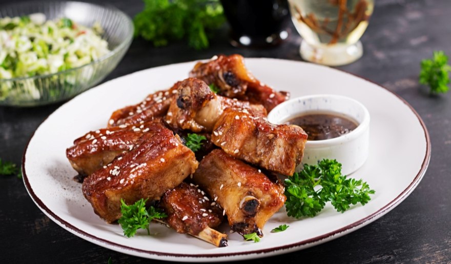Barbecue ribs on a plate, accompanied by sauce and a fresh salad, featured at Swig & Swine in Myrtle Beach.