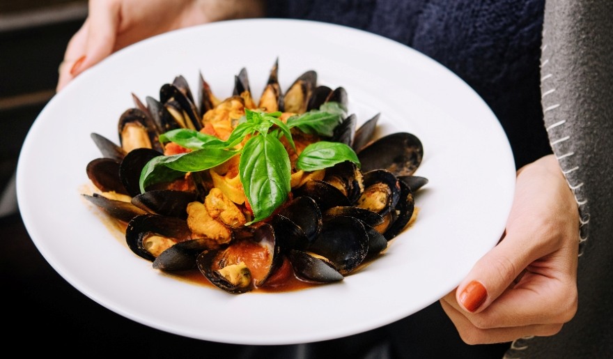 A woman presents a plate of mussels, highlighting a seafood offering at The Library Restaurant in Myrtle Beach.