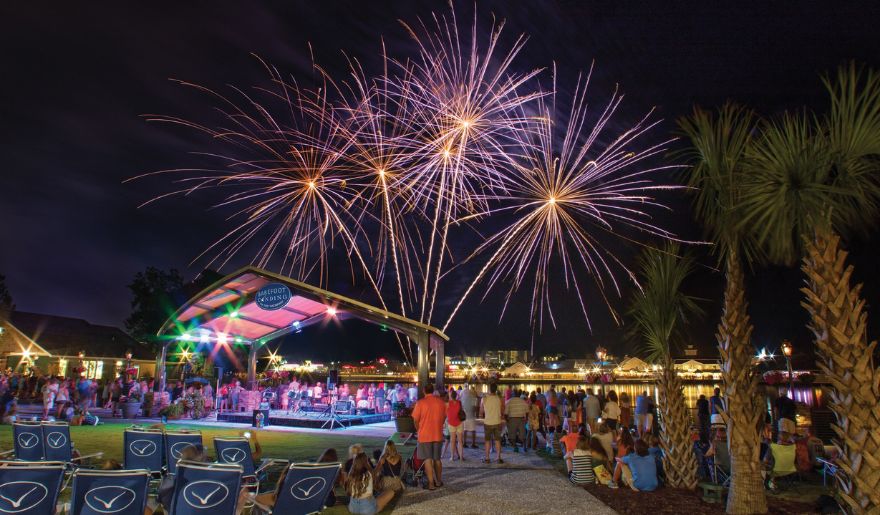 Colorful fireworks illuminate the night sky over water, with families enjoying the view from Barefoot Landing at Myrtle Beach.