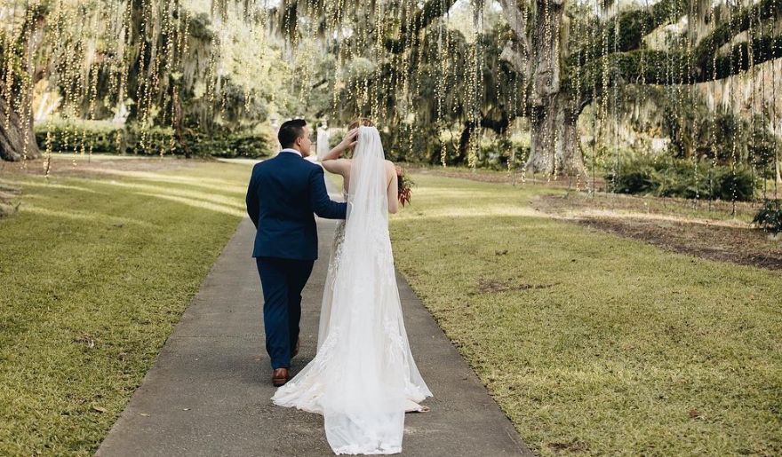 A couple in wedding attire walks through the picturesque Brookgreen Gardens, blending art and nature in Myrtle Beach.