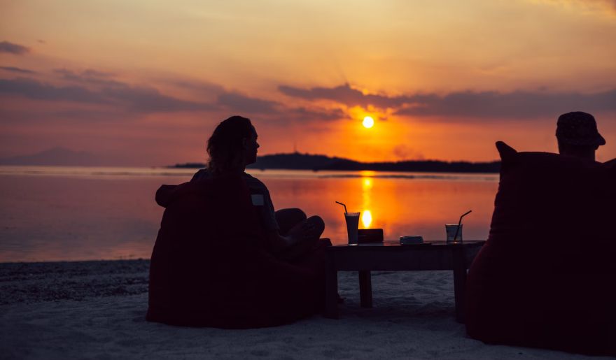 A couple sits at the beach, savoring sunset cocktails as the sun sets over Myrtle Beach.