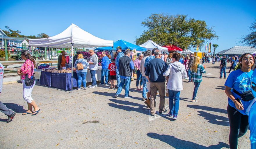 Couples and individuals enjoy an outdoor market, surrounded by colorful stalls and a bustling, cheerful environment.