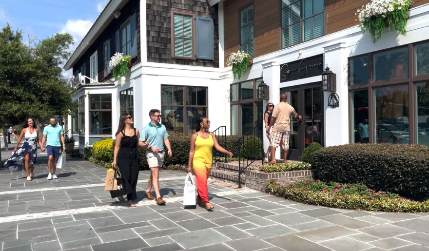 Couples stroll along the sidewalk outside a store in North Myrtle Beach, enjoying a day of shopping together.