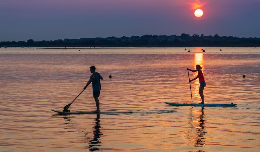 The couple paddle boarding on calm waters during a picturesque sunset, capturing a romantic moment in Myrtle Beach.