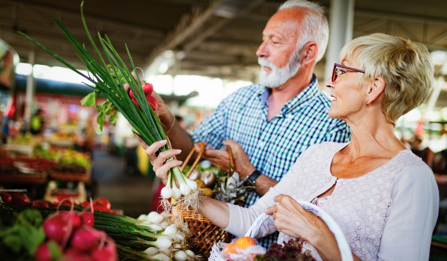 A senior couple explores a farmers market, selecting fresh fruits and vegetables in Myrtle Beach.
