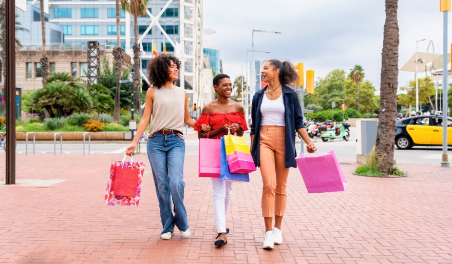 Three women walk along a street in Myrtle Beach, each holding shopping bags, embracing the Spring Break shopping experience.
