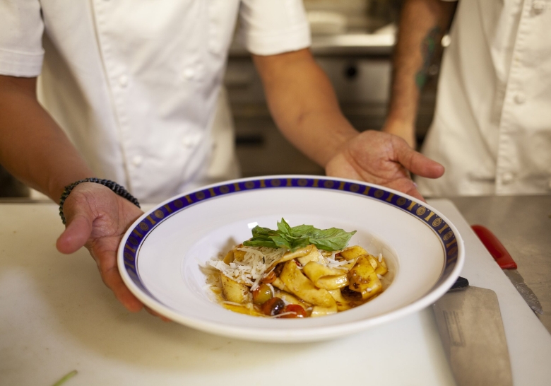 A chef presents a bowl of food over a counter, showcasing culinary expertise in a vibrant kitchen setting.