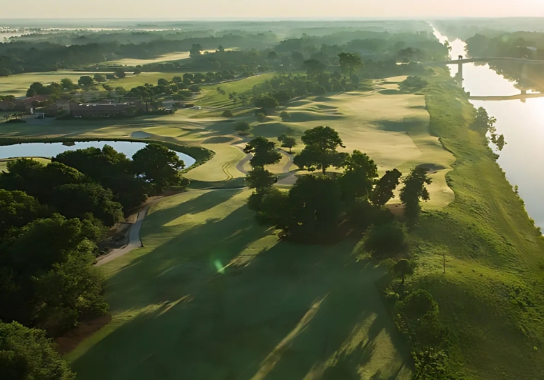 Aerial view of a golf course featuring water and trees, highlighting the scenic landscape near Myrtle Beach condos for rent.