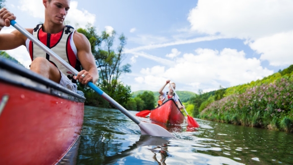 A group of people enjoys paddling a canoe down a river, enjoying watersports in Myrtle Beach's scenic environment.