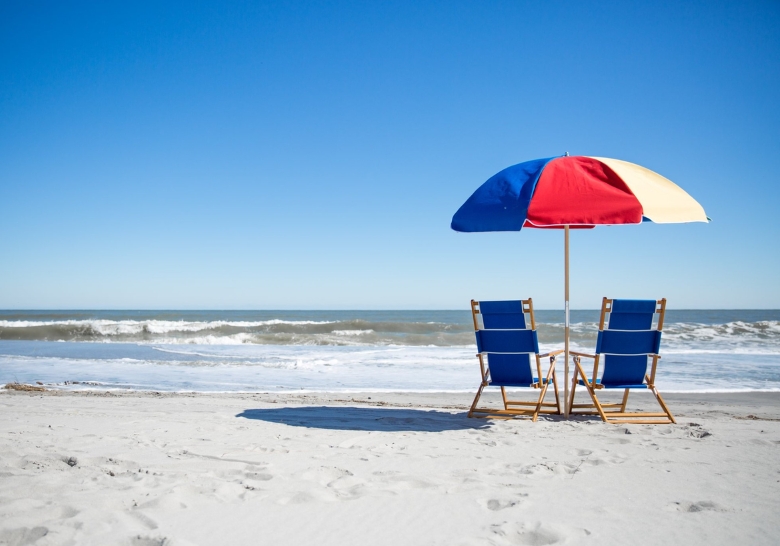 A serene beach scene featuring two chairs and an umbrella, inviting relaxation at Myrtle Beach's exclusive condo rentals