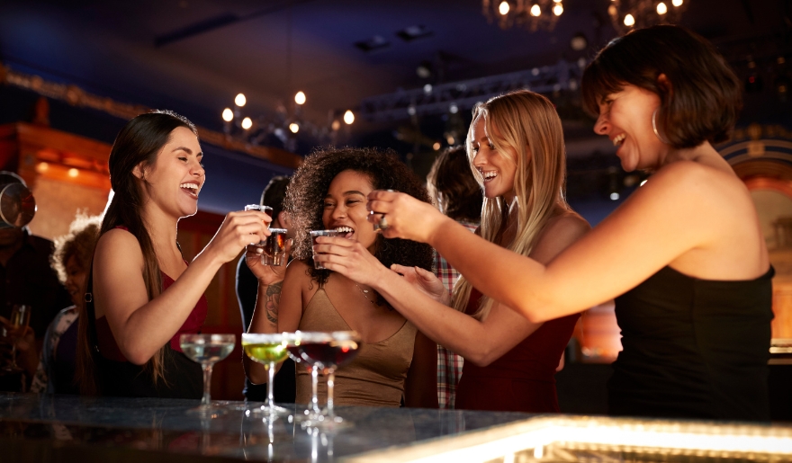 A group of women joyfully toasting with cocktails at a bar during a Myrtle Beach bachelorette party celebration.