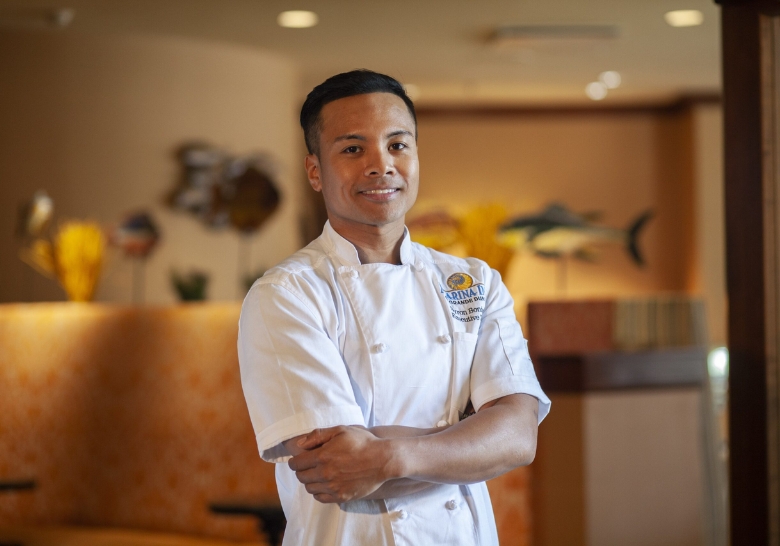 A man in a white chef's uniform stands proudly in front of a restaurant, promoting the Myrtle Beach Easter Brunch menu.