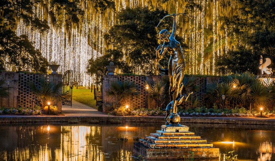 A statue illuminated by lights stands in the center of a tranquil pond during Myrtle Beach's Night of a Thousand Candles event.