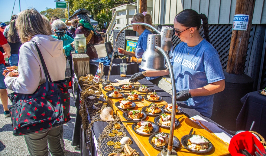 A group of people gathered around a table filled with food at the Taste of the MarshWalk event in Myrtle Beach.