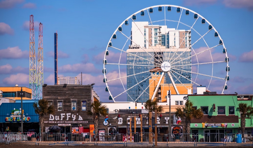 A Ferris wheel stands in front of the Myrtle Beach SkyWheel building, showcasing a family vacation scene.