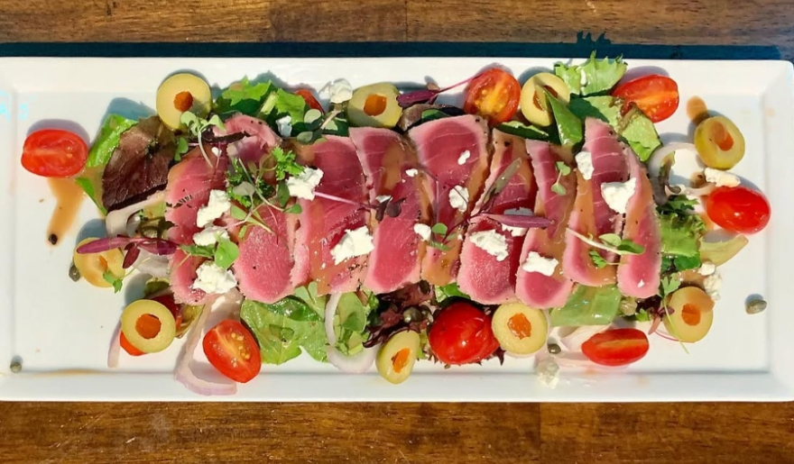 A fresh salad featuring tuna, tomatoes, and olives served on a white plate at Pine Lakes Tavern, Myrtle Beach.