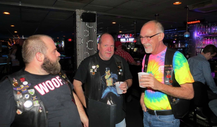 Three men in biker shirts engaged in conversation at the Pulse Ultra Club bar in Myrtle Beach nightlife.