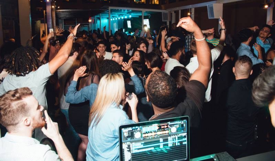 A vibrant party scene at RipTydz Rooftop Bar in Myrtle Beach, showcasing a group of people and DJ equipment in action.