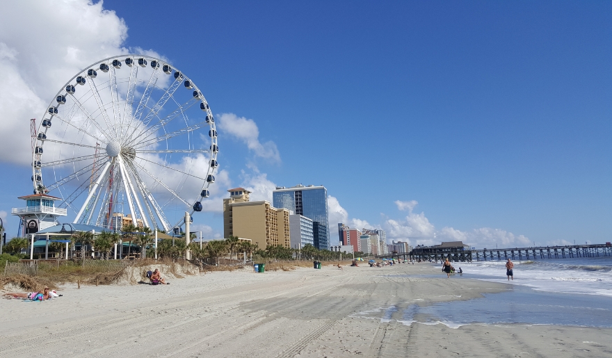 A colorful ferris wheel overlooks Myrtle Beach, where visitors relax on the Grand Strand in the warm sun.