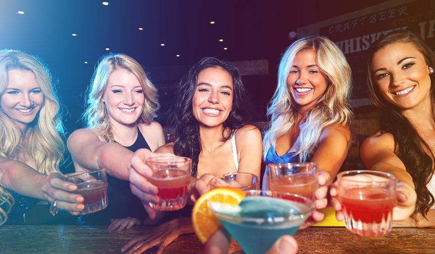 A group of smiling friends toasting with colorful cocktails at a lively bar, capturing the energy of Myrtle Beach nightlife. 