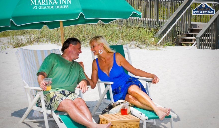 A couples relax on beach chairs under an umbrella, enjoying their honeymoon at Myrtle Beach's Marina Inn.