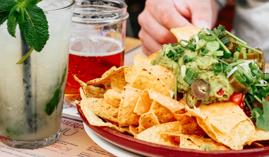 Nachos with melted cheese and toppings alongside a drink on a table, showcasing Myrtle Beach's Nacho Hippo atmosphere.