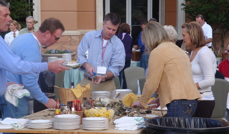 A group of people gathered around a table filled with plates and bowls, showcasing social events in Myrtle Beach.