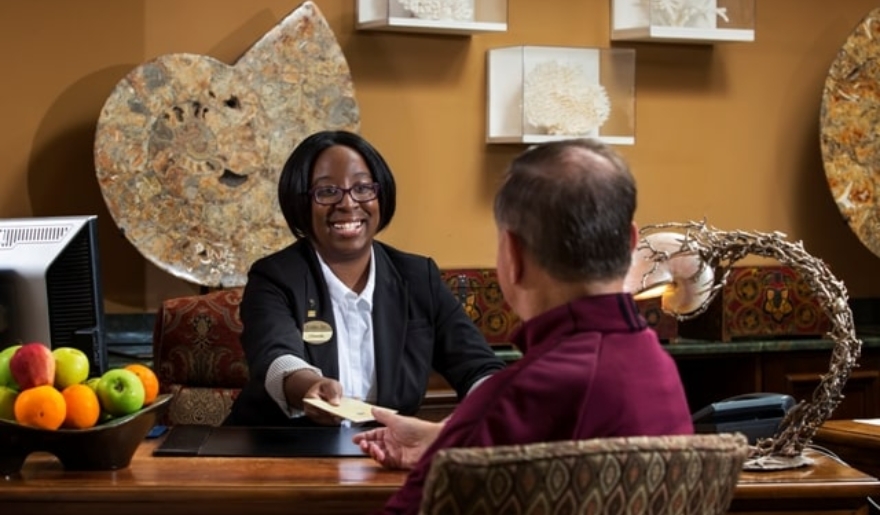 A smiling woman interacts with a receptionist at a hotel, focusing on event planning at Marina Inn at Grande Dunes, Myrtle Beach.