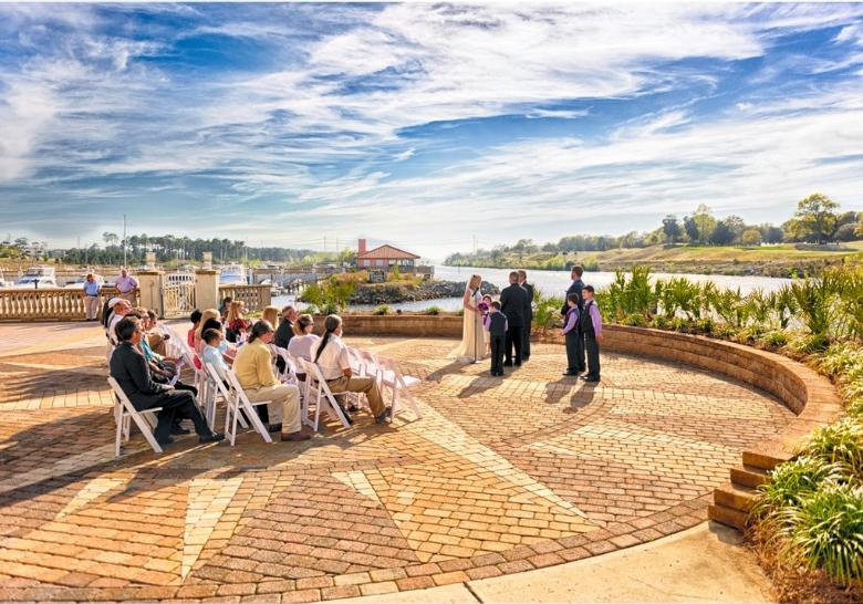 A wedding ceremony takes place on the waterfront at Marina Inn in Myrtle Beach, SC, with guests seated and a beautiful ocean backdrop.