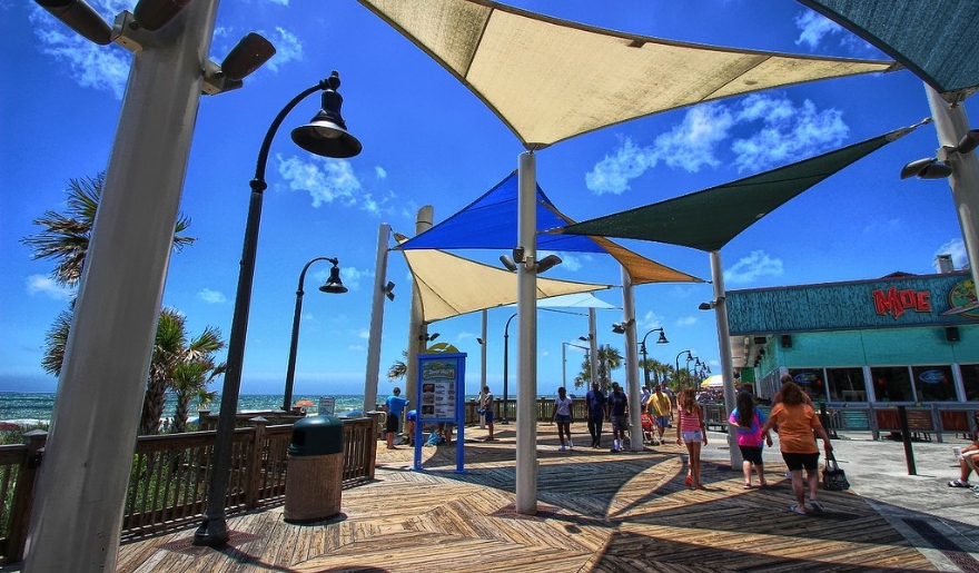 People stroll along the Myrtle Beach Boardwalk on a sunny August day, enjoying the beach atmosphere.