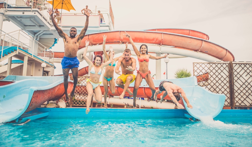 A group of people joyfully jumping into the water from a colorful water slide at Myrtle Beach in August.