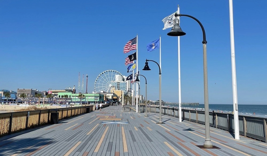 A vibrant Myrtle Beach boardwalk in June, featuring colorful flags and a towering Ferris wheel against a clear sky.