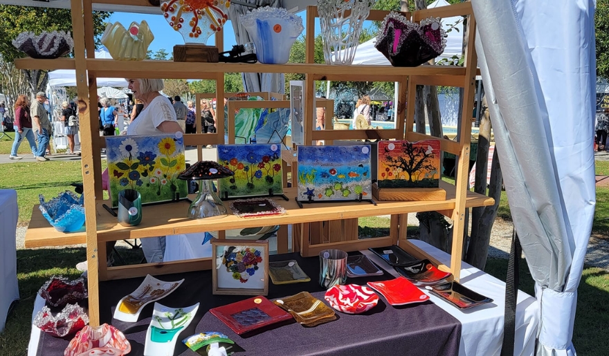 A display table showcasing numerous art pieces under a tent at Myrtle Beach Art in the Park during June.