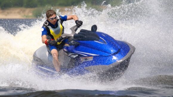 A man riding a blue jet ski fast through the water, creating large splashes.