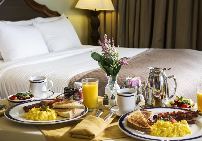 A romantic hotel room featuring a bed and a beautifully arranged breakfast for two, perfect for a honeymoon in Myrtle Beach.